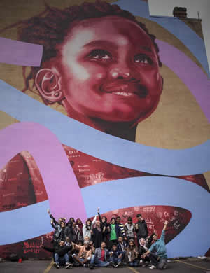 Students waving arms and standing in front of a mural