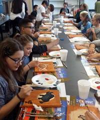 students sitting at long table painting
